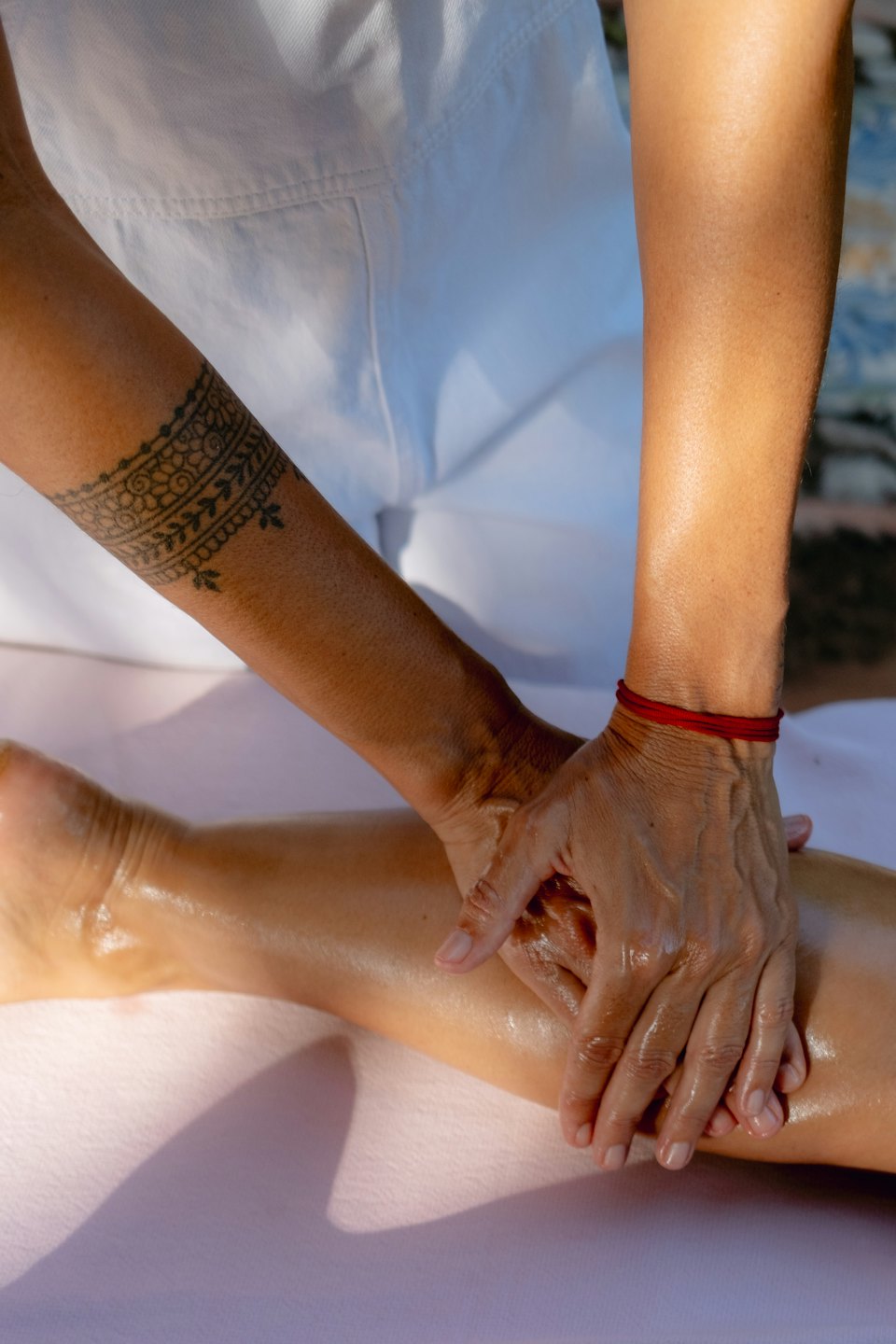 Therapeutin mit Tattoo gibt einer Klientin eine Öl-Beinmassage.